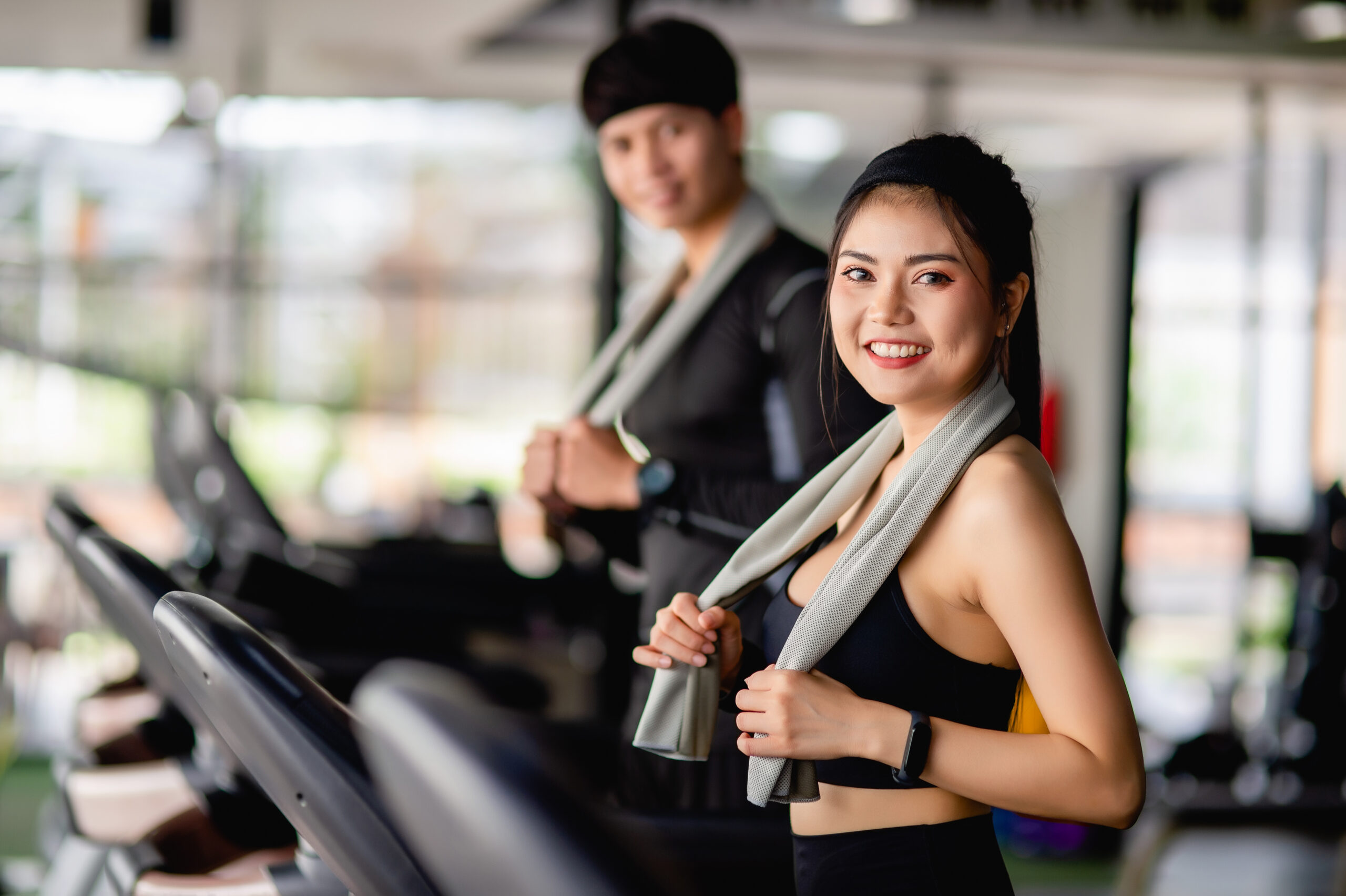 Young fit man and woman running on treadmill in gym.
